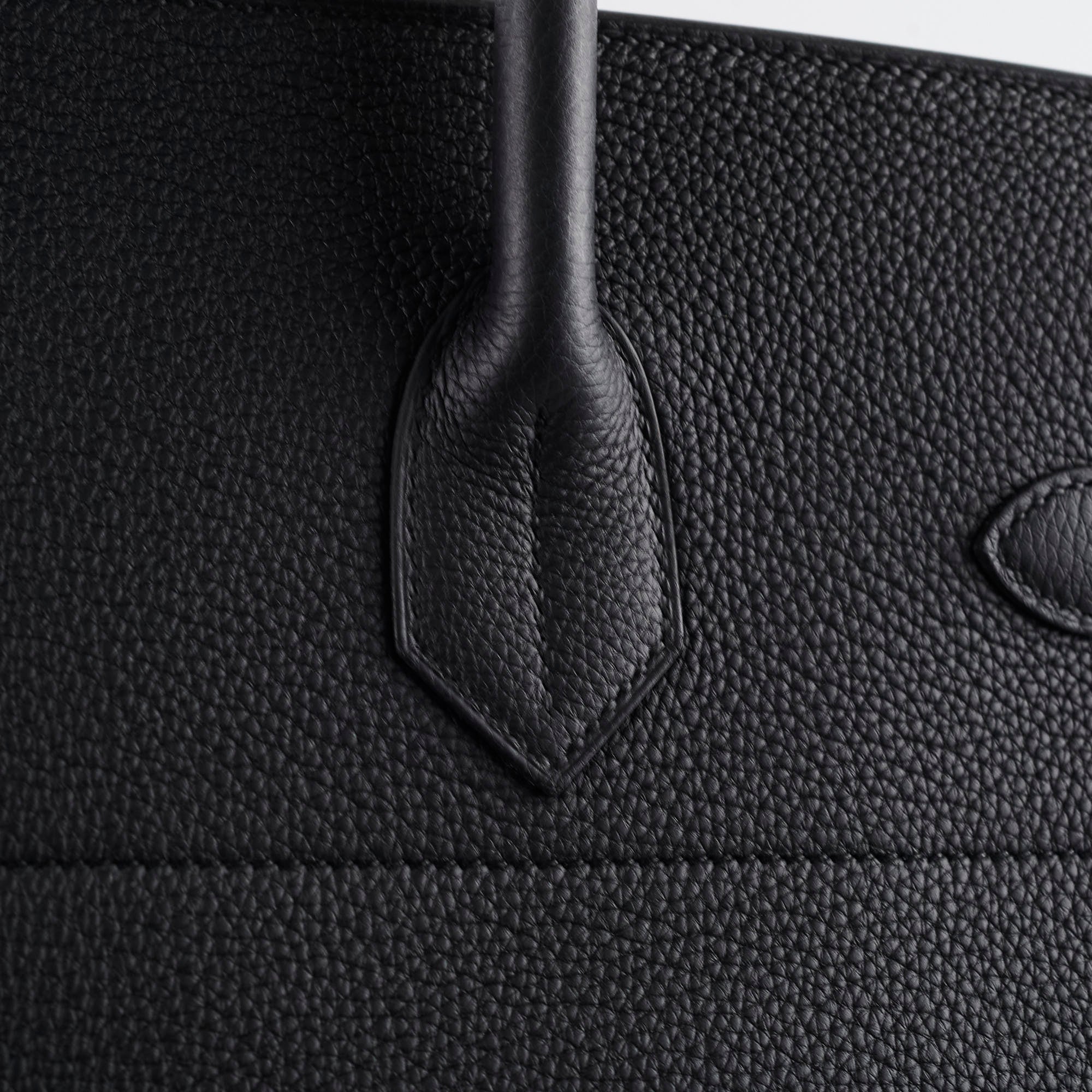 Close-up of a black textured leather bag with a handle.