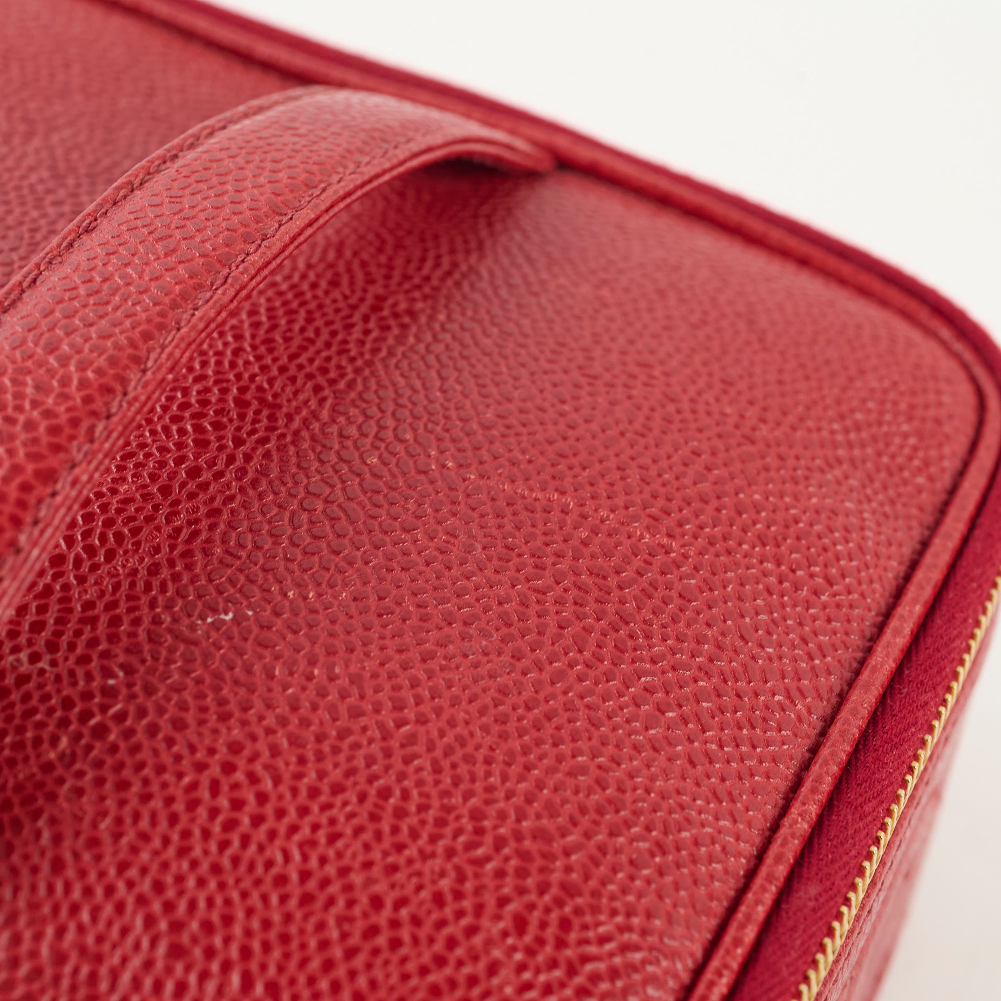 Close-up of a red textured leather product with a gold zipper.