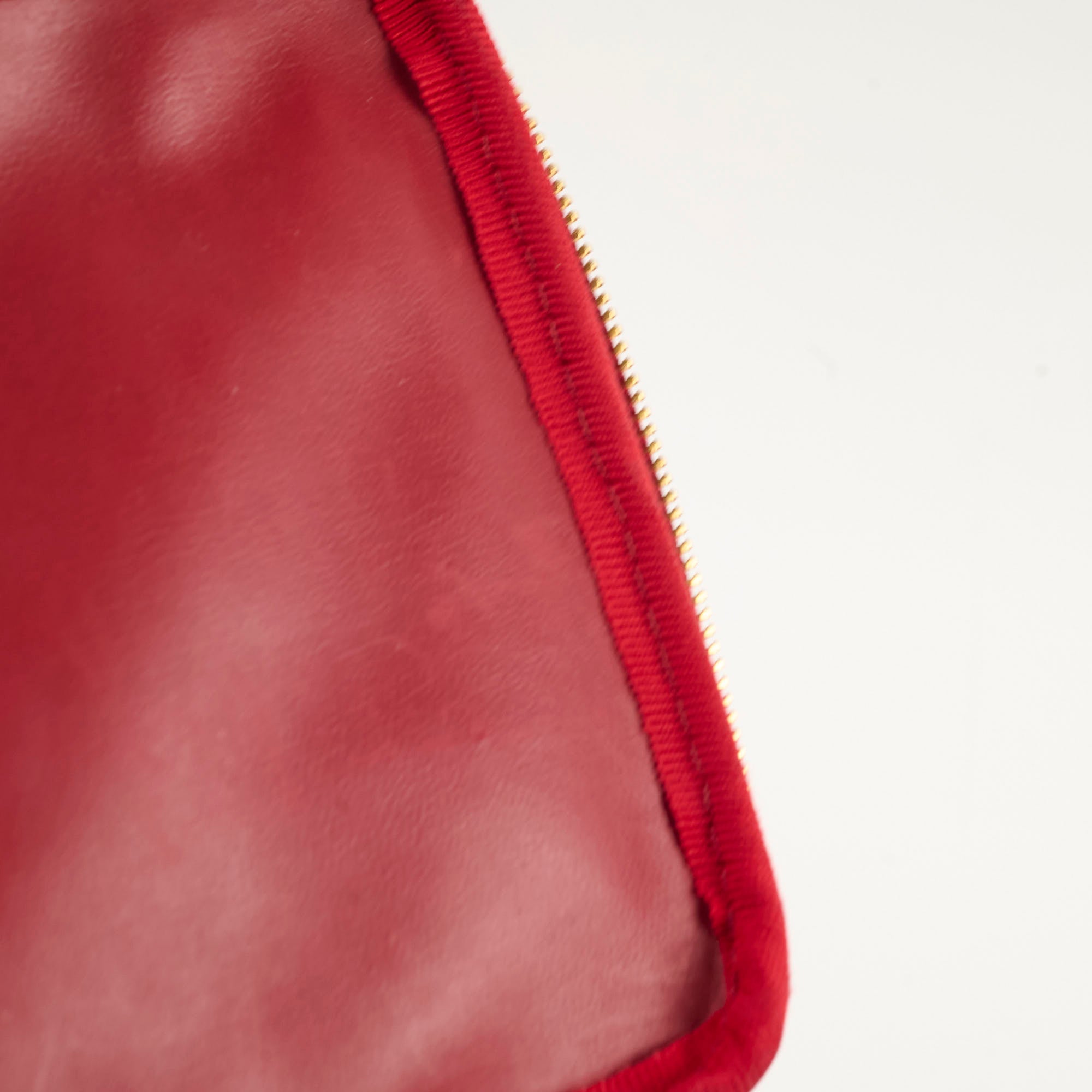 Close-up of a red leather product with a gold zipper 
