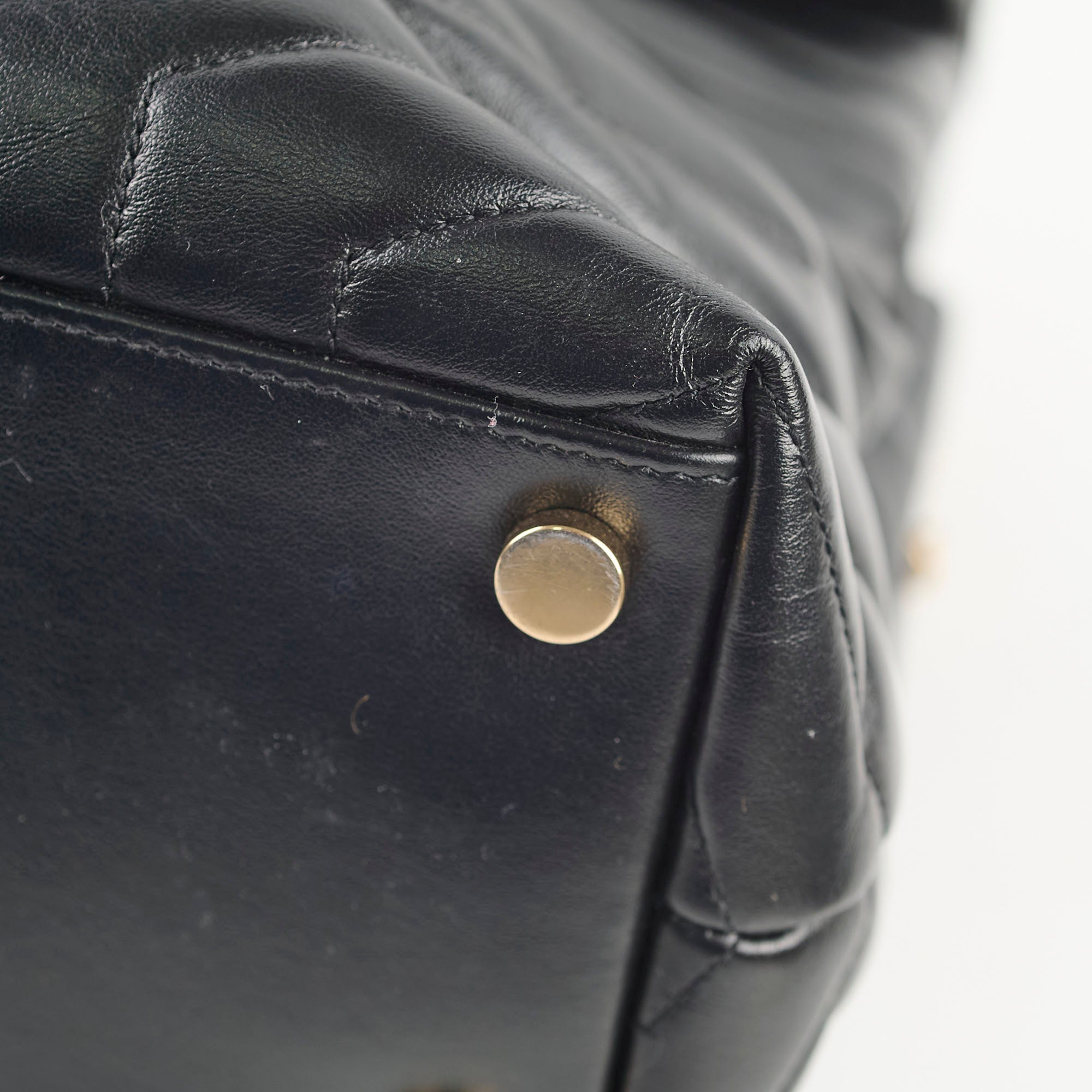 Close-up of a black leather bag with a gold metal button.