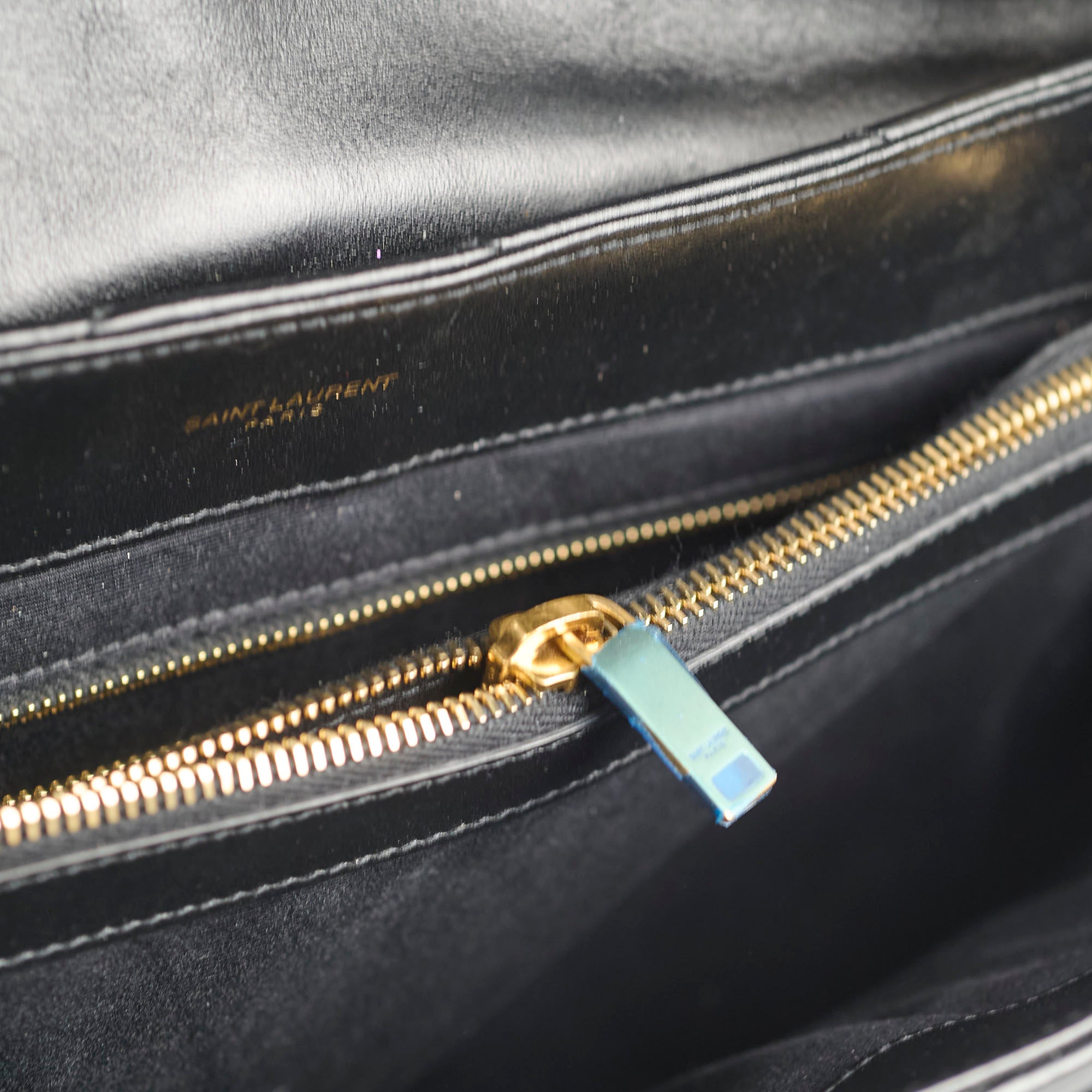 Close-up of a black leather bag with gold zipper and Saint Laurent branding.