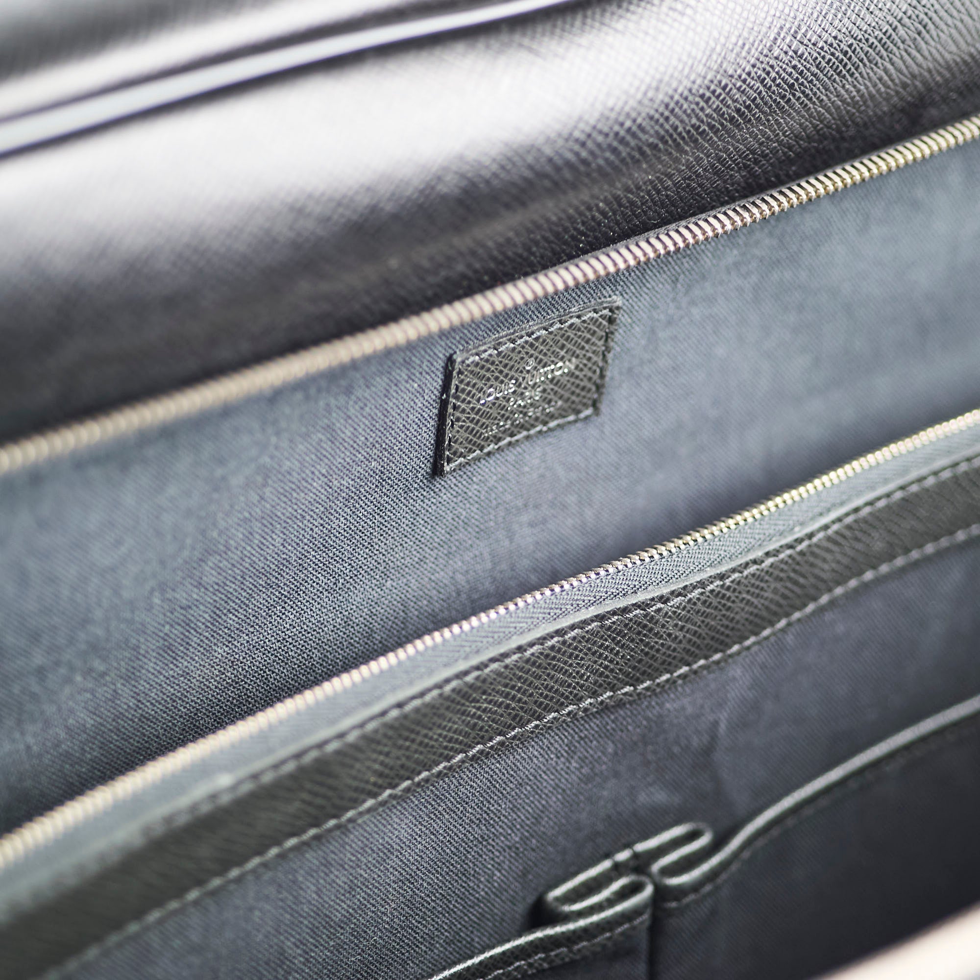 Close-up of a dark gray bag with a brand logo on a matching gray background